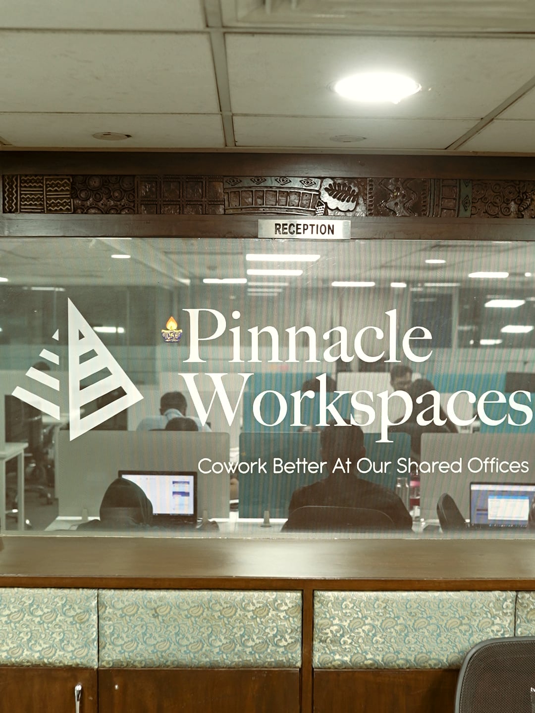 The etched Pinnacle Workspaces wordmark on the reception glass, with the open floor beyond it
